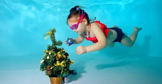 baby swimming in a pool with a Christmas tree